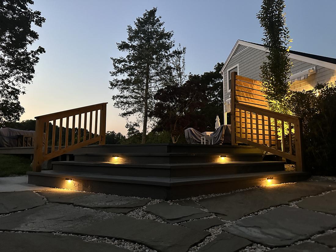 Deck stairs and a stone patio with step lights at dusk