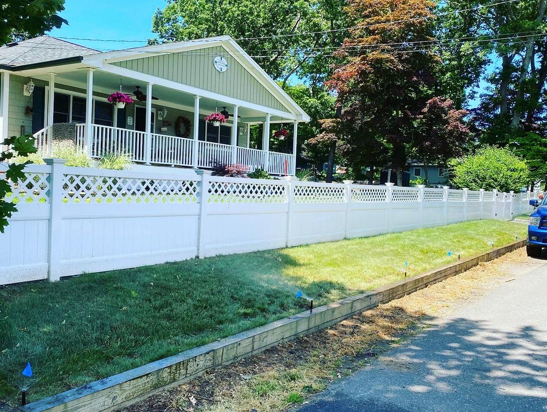Green lawn along a white fence in front of a house with a porch