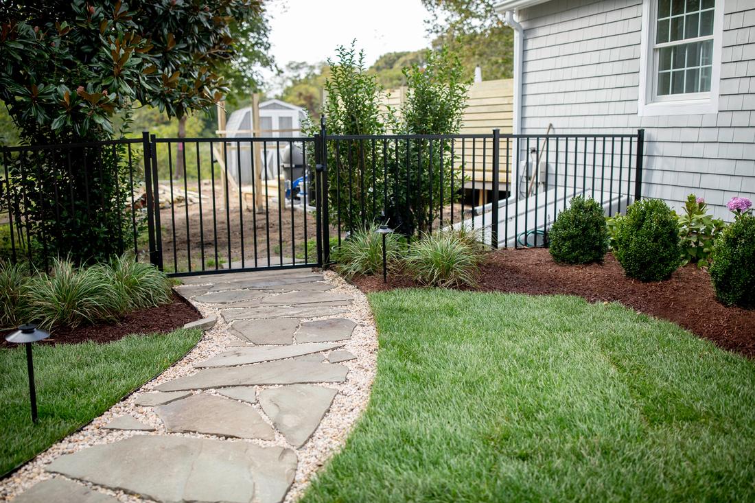 Stone path and garden gate with path lights in daylight