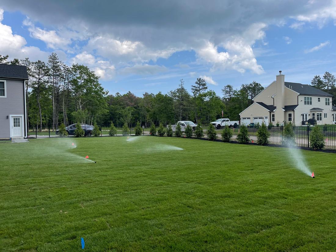 Rotor sprinklers watering a wide front lawn in front of a new house