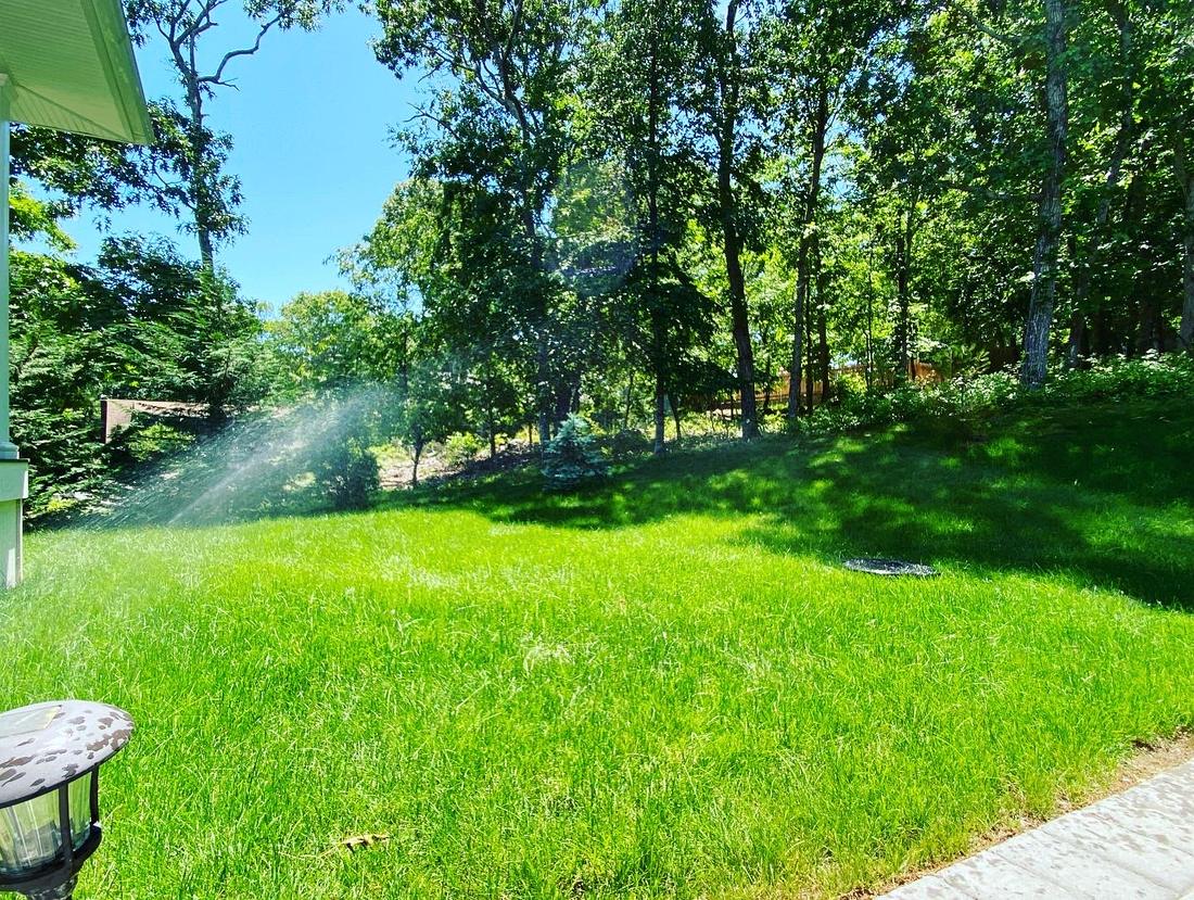 Sprinkler running beside a stone walkway on a green lawn