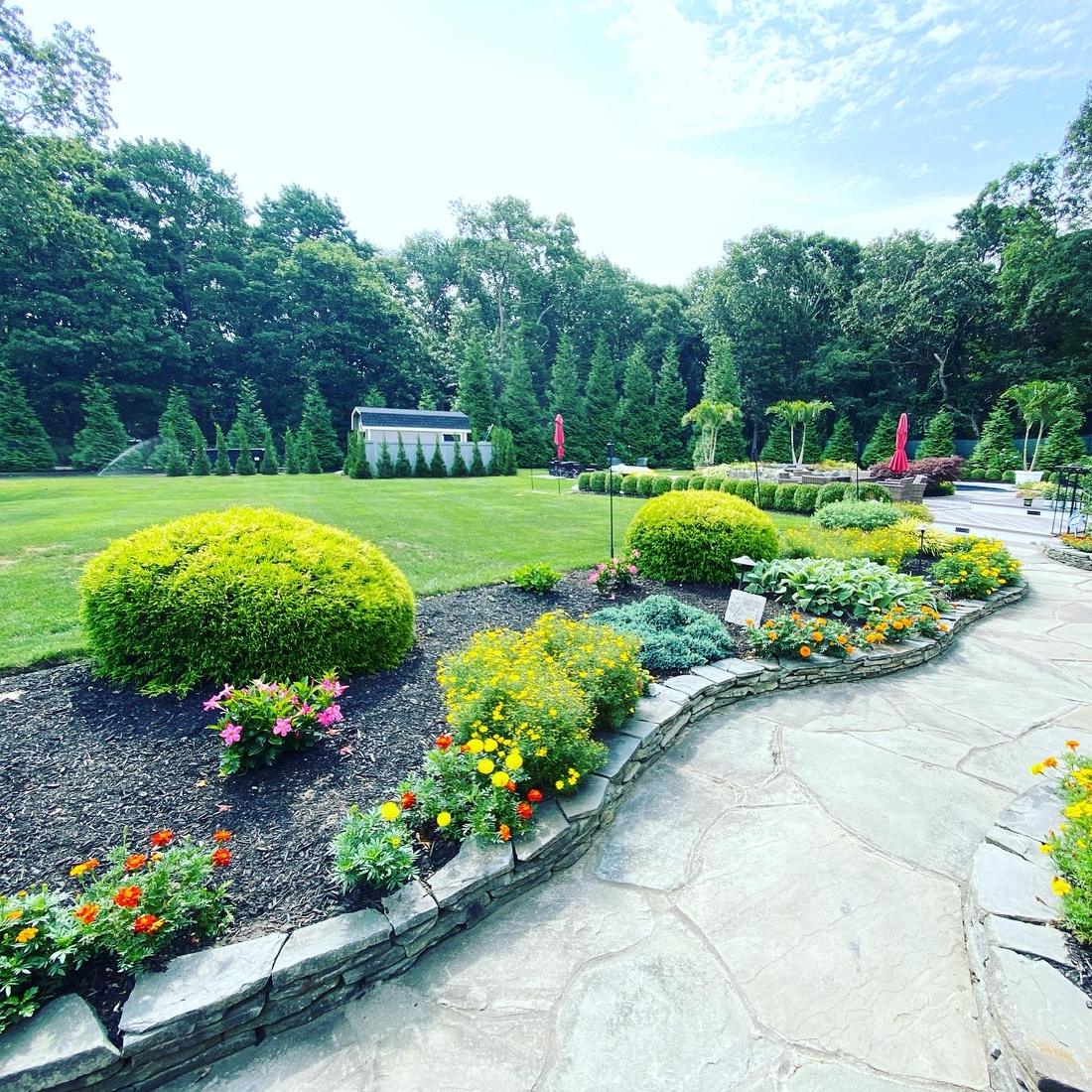 Flagstone path curving past flower beds and a green lawn